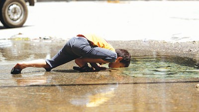 صورة مؤثرة .. طفل سوري يشرب من المياه المتجمعة على أرضية الشارع